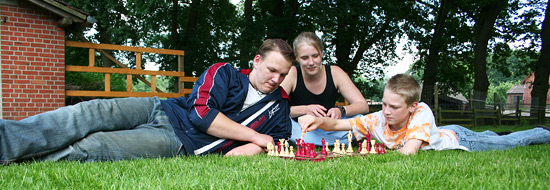 Darstellung davon drei Personen die auf einer Wiese Schach spielen